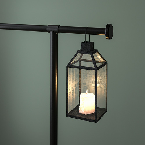 Un farol colgante con una vela encendida en su interior, suspendido de una varilla decorativa sujeta a una mesa.