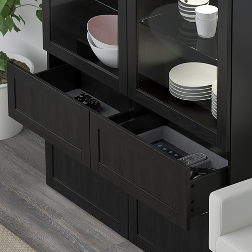 Mueble BESTÅ negro con cajón abierto que muestra el control remoto y puertas de vidrio que muestran platos y tazones.