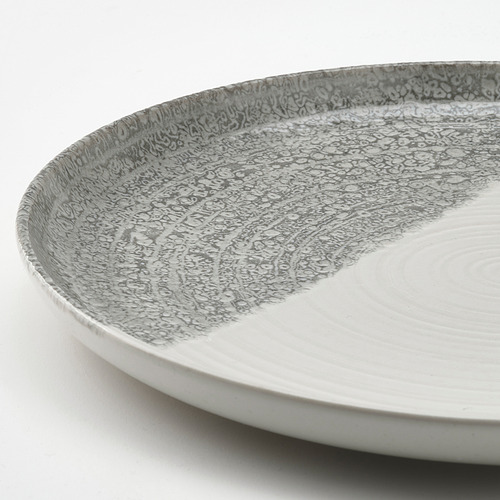 Plato distintivo en blanco y gris con un esmalte texturizado, que muestra un efecto de inmersión.