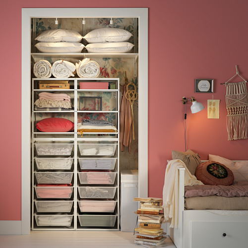 Estanterías JONAXEL con almohadas, sábanas y cojines, libros y cama contra paredes rosas.