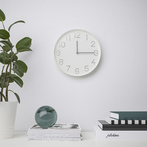 Reloj blanco moderno con agujeros numéricos negros en la pared, revistas con esfera de vidrio, planta cerca.