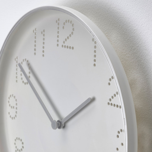 Primer plano de un moderno reloj de pared blanco con diseño de números perforados, manecillas minimalistas.