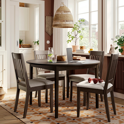 Modern farmhouse dining set with dark gray round table and 4 cushioned chairs, placed on a multicolored rug under a large window.