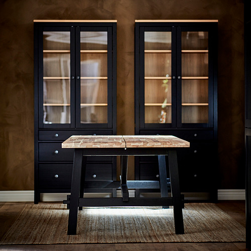 Moderna mesa de centro negra con tapa de madera, flanqueada por armarios negros a juego con puertas de cristal. Ambiente acogedor y elegante.