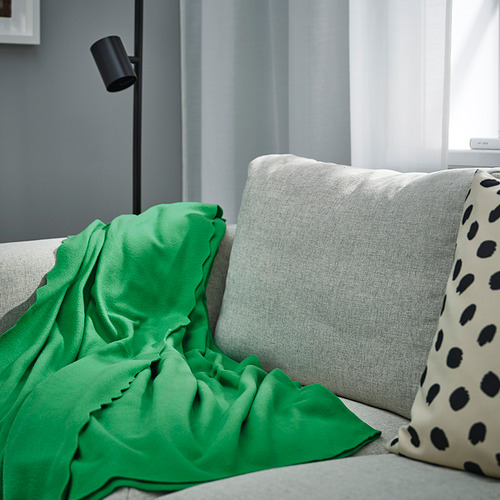 Una acogedora manta verde DAGGKÅPOR sobre un gran sofá gris, que complementa una almohada con manchas.
