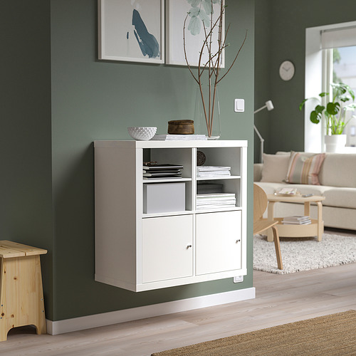 Estantería KALLAX blanca contra una pared verde, que sostiene libros y artículos de decoración. Su tamaño compacto encaja bien con la decoración de las habitaciones.