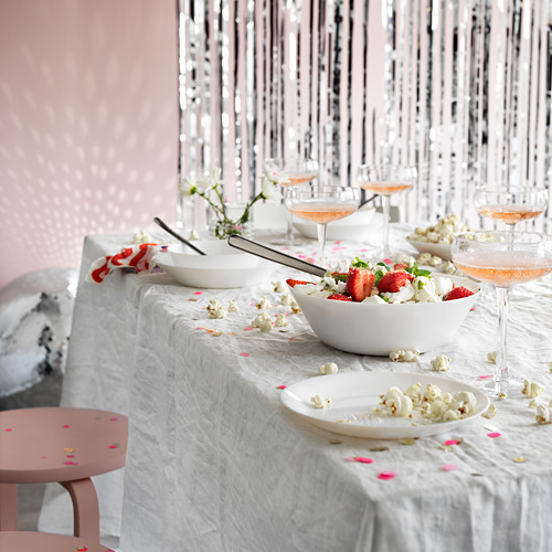 Elegante configuración de mesa con tazones de vidrio templado blanco, palomitas de maíz, fresas y vasos cupé. Serpentinas plateadas decoran el fondo.