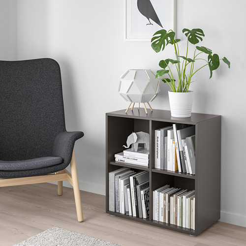 Dark grey EKET unit with books & plant, beside grey chair on light wood floor.