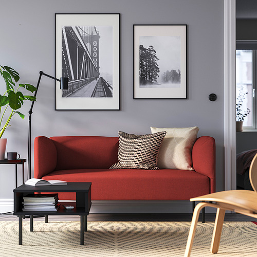 Modern living room with red LILLEHEM sofa, patterned pillows, black coffee table, art prints, floor lamp, and potted plant.