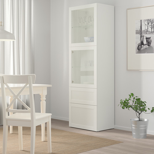 Mueble blanco BESTÅ con puertas de cristal, alto, delgado, entre silla y cuadro enmarcado.