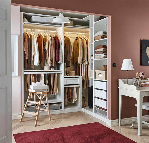 Moderno vestidor con perchas, estantes y cajones en color blanco, organizados de manera ordenada. Una alfombra roja está en el suelo.