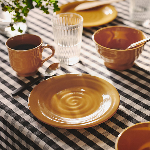 Platos y tazas de cerámica de color amarillo ocre sobre mantel de cuadros. Pequeño, rústico, hecho a mano.
