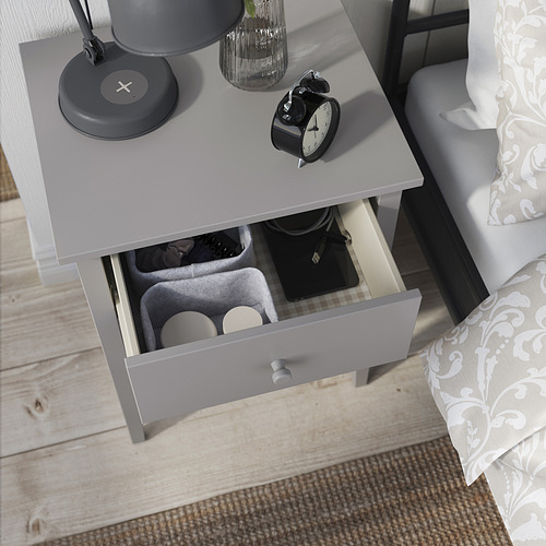 Mesita de noche GULLABERG blanca con cajón abierto, lámpara, reloj y decoración.