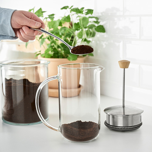 Una persona vierte posos de café en una jarra de vidrio transparente, parte de la serie IKEA 365+, junto con un émbolo para hacer café.