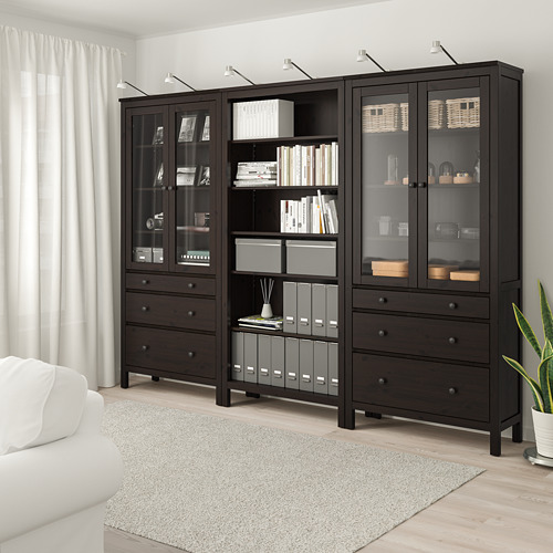 Mueble de almacenaje HEMNES marrón oscuro con estantes y cajones, junto a sofá blanco.