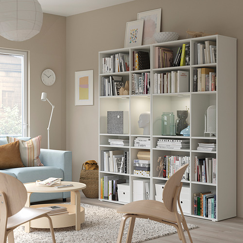Estantería blanca con libros, decoración, silla y sofá azul en una elegante sala de estar.