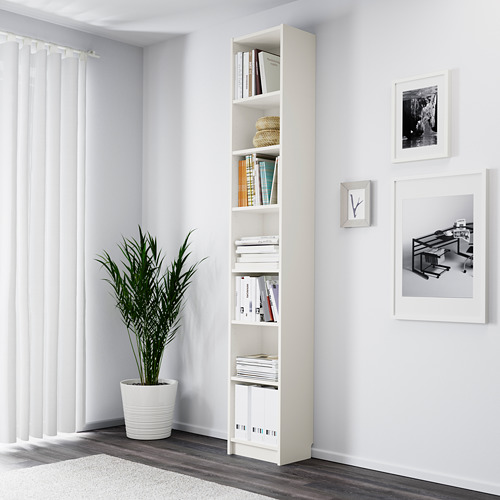 Una estantería blanca alta llena de libros, una cesta de mimbre y decoración. Está colocado en una esquina junto a una planta alta y verde en maceta.