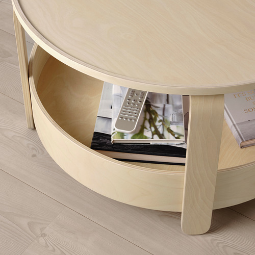 Mesa de centro redonda de madera clara con estante de almacenamiento, soporte para control remoto y libros.