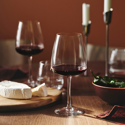 Copa de vino y queso sobre tabla de madera, velas sobre la mesa.