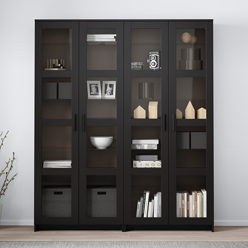 Una vitrina negra BRIMNES con puertas de cristal, que muestra libros y decoración.
