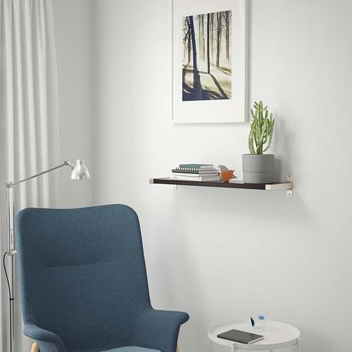 Un rincón de lectura minimalista con estantería, planta, libros, figurita, silla, lámpara y mesa con tableta.