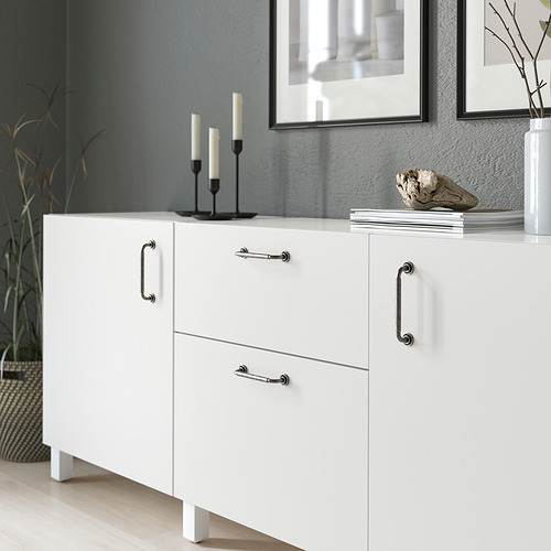 Mueble blanco con tiradores antiguos, donde se exhiben elementos decorativos, como candelabros y libros.