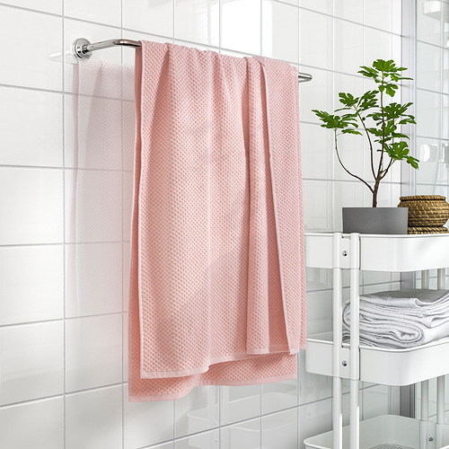 Toallero scroll con toalla GULVIAL texturizada de color rosa claro junto a la unidad de almacenamiento y la planta blancas.