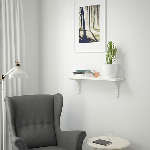 Rincón minimalista con silla gris, mesa redonda, tableta, cristal, estantería de pared con cactus, libros y estampado de la naturaleza.