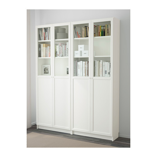 Librería blanca BILLY con puertas de cristal, mostrando estanterías llenas de libros y artículos de decoración.