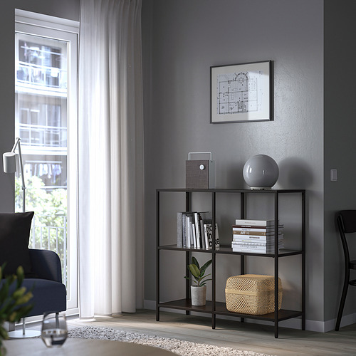Sala de estar moderna con estantería VITTSJÖ, libros, lámpara, planta y silla azul junto a la ventana.