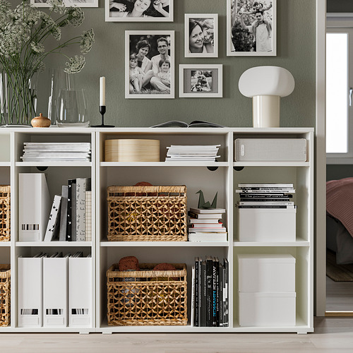 Sala de estar moderna con estantes de almacenamiento VIHALS blancos, que contienen libros, cestas y fotos. Una lámpara blanca y una planta están en la parte superior.