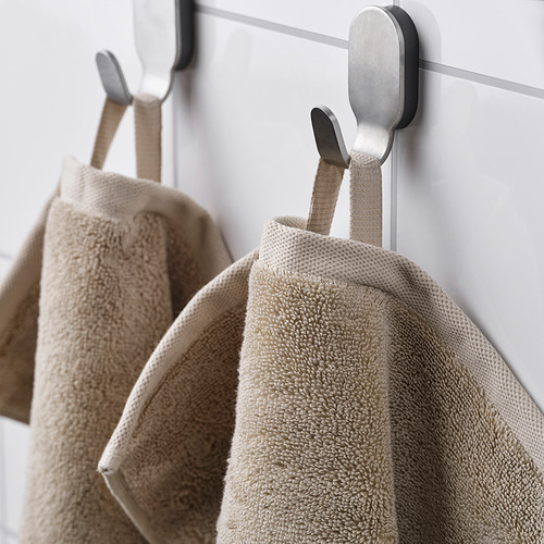 Dos toallas beige cuelgan cuidadosamente de ganchos metálicos, mostrando su textura suave y almacenamiento organizado.
