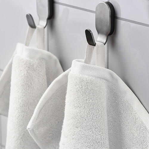 Toallas blancas sobre ganchos, suaves y absorbentes, pared gris.