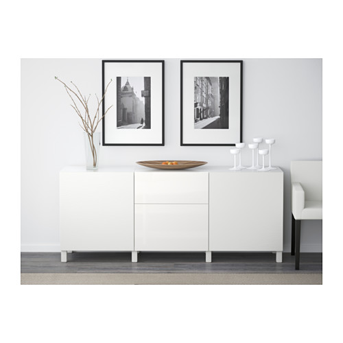 Aparador blanco con cajones y estantes. Arte enmarcado en blanco y negro arriba. Cuenco, vasos y jarrón decorativo en la parte superior.