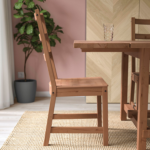 Silla de madera con asiento en ángulo, respaldo alto, distribución uniforme del peso. En la mesa, plante cerca.