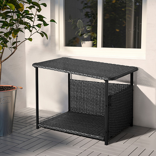 Mesa de exterior de mimbre, gris oscuro, rectangular con patas metálicas, cerca de ventana y papelera.