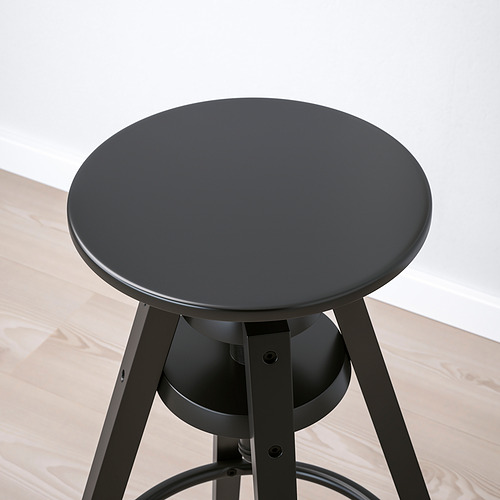 Taburete redondo negro regulable en altura sobre suelo de madera. Diseño moderno con robustas patas metálicas y asiento liso.