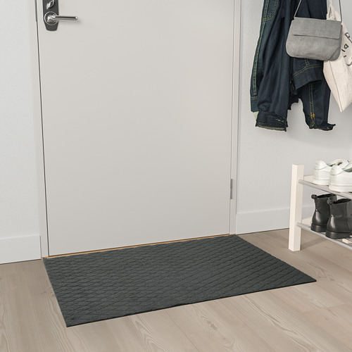 Alfombrilla ÖSTERILD gris cerca de puerta blanca, poliéster reciclado, texturizado.
