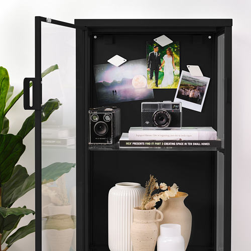 Un armario con puerta de cristal negro con fotos unidas por imanes, que muestran cámaras y jarrones.