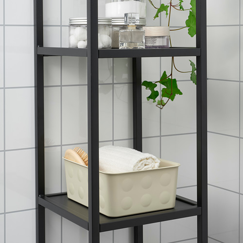 Estante de metal negro con contenedor blanco que almacena toallas, frascos y plantas contra la pared de azulejos blancos.