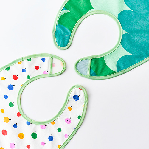 Tres coloridos baberos infantiles con parte delantera impermeable y parte trasera de algodón suave, diseñados con patrones divertidos y ribetes verdes.