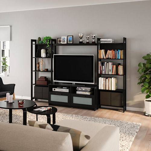 Moderno mueble de TV negro y estantes con plantas, trofeos, libros. Sofá beige, suelos de madera, minimalista.