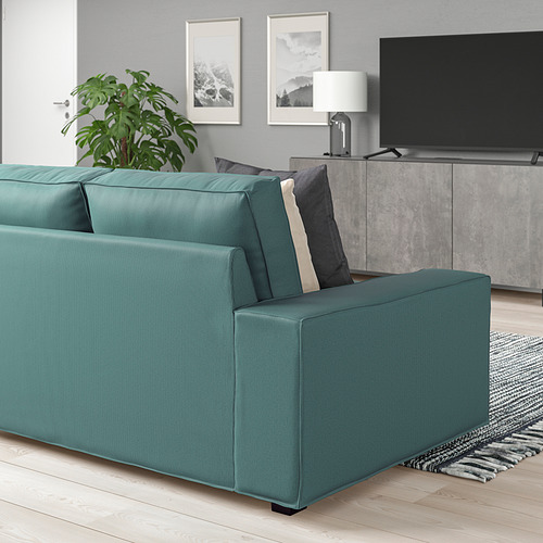 Sofá KIVIK verde azulado, tv, consola gris, alfombra negra, planta en salón minimalista.