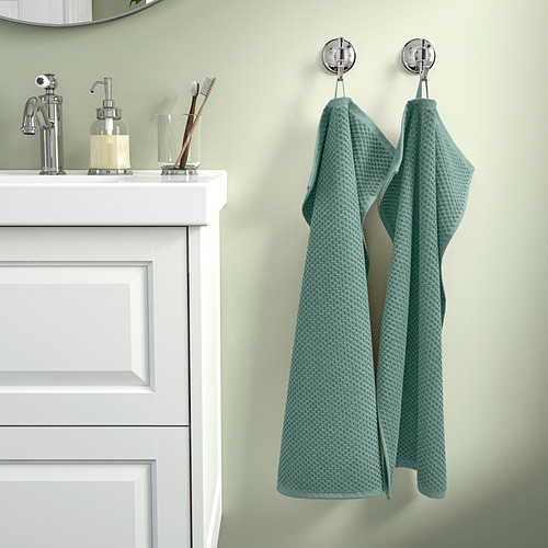 Baño con armario blanco, lavabo y toalla GULVIAL verde azulado con ganchos.