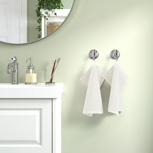 Baño con paredes verdes, armario blanco, lavabo cromado, toallas en ganchos.