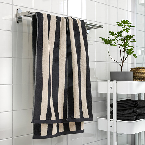 Toalla de rayas negras y beige en estante de metal en baño limpio.