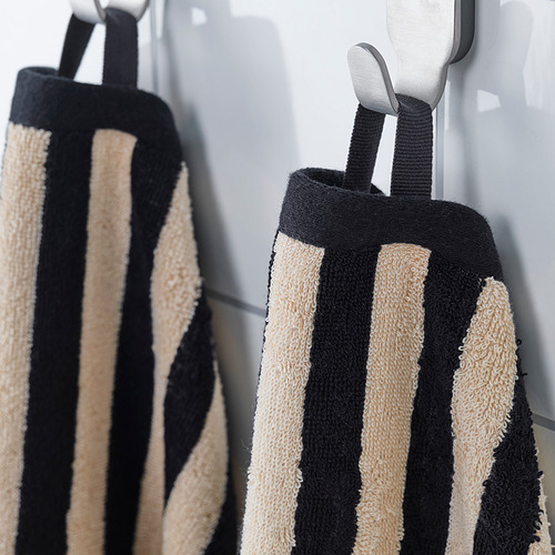 Las toallas de rayas negras y beige cuelgan cuidadosamente en ganchos, mostrando su diseño absorbente y elegante.