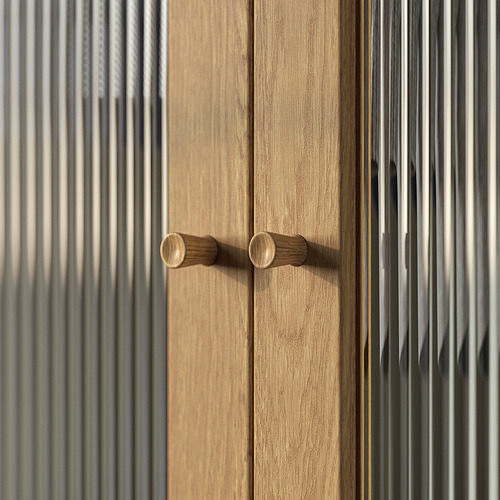 Un primer plano de la puerta de un armario de madera con dos tiradores cilíndricos en acabado natural. Los patrones verticales de vetas de madera de la puerta.