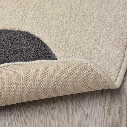 Esquina de alfombra beige con reverso de goma texturizada y antideslizante. Material suave y duradero para el juego de los niños.