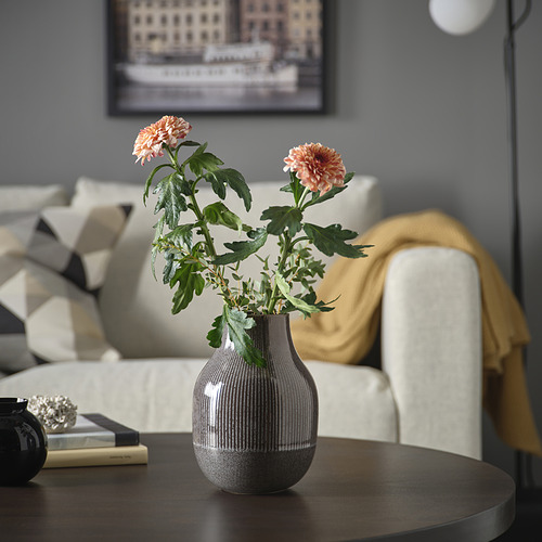Jarrón GRADVIS con flores rosas, cuenco, libros y sofá.